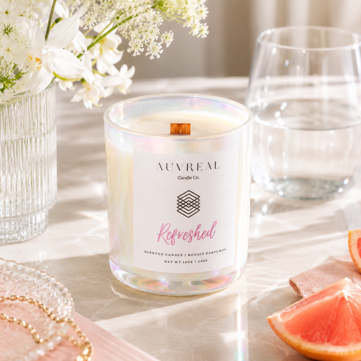 Auvreal candle labeled 'Refreshed' on a table with flowers, a glass, and fruit.